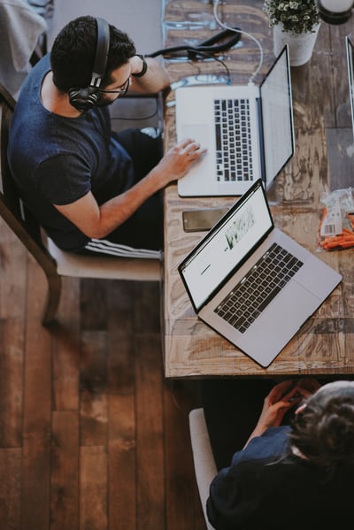 A student with headphones working at a table on his laptop. A student with headphones working at a table on his laptop.